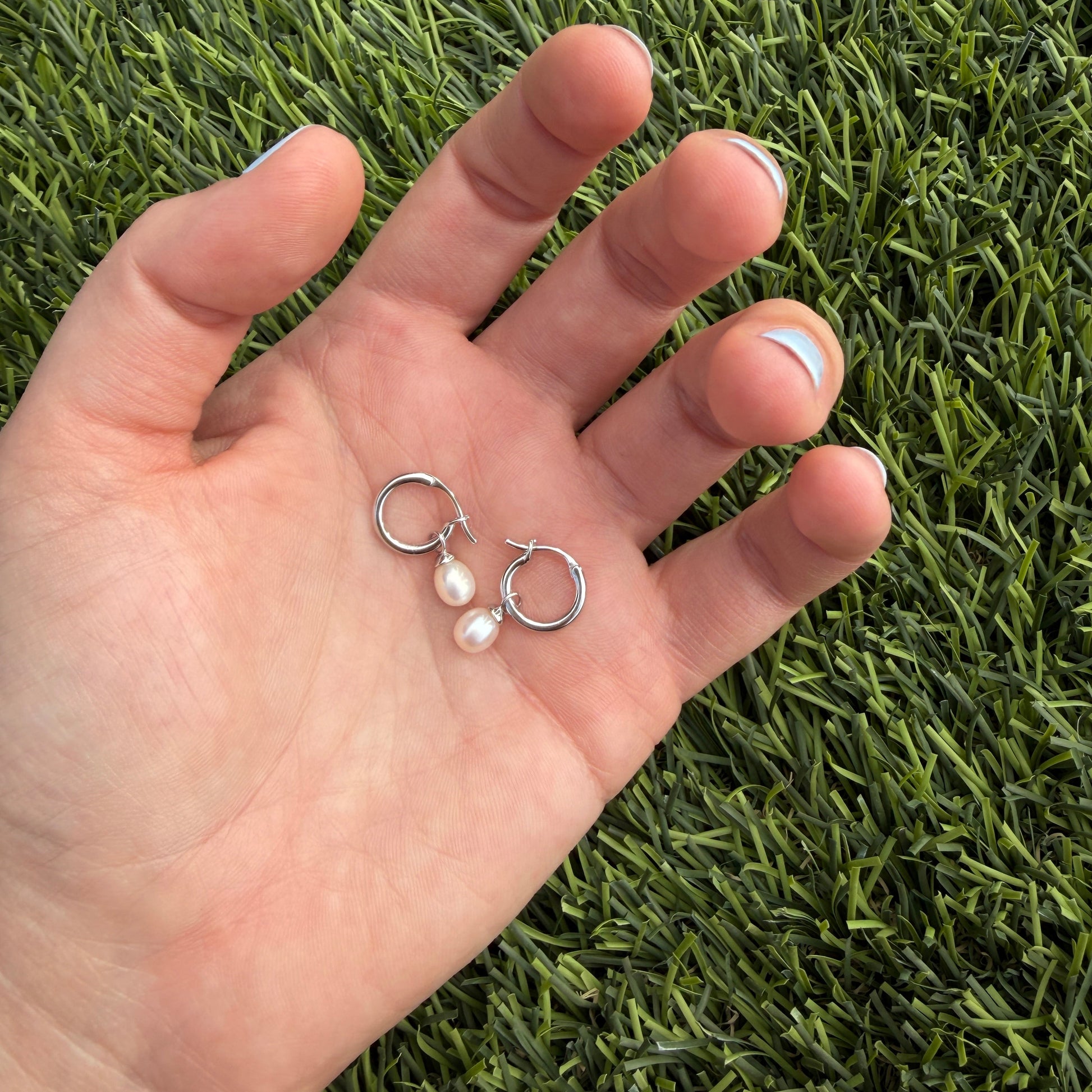 Hand holding two small earrings against a grass background