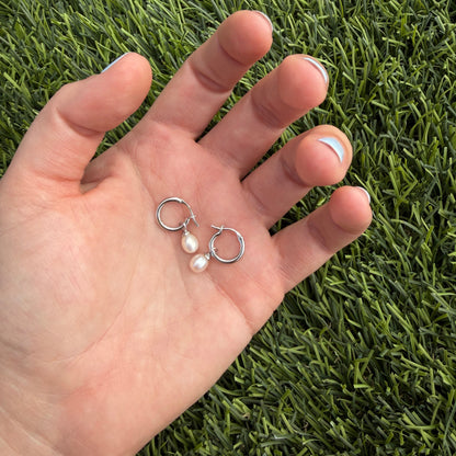 Hand holding two small earrings against a grass background