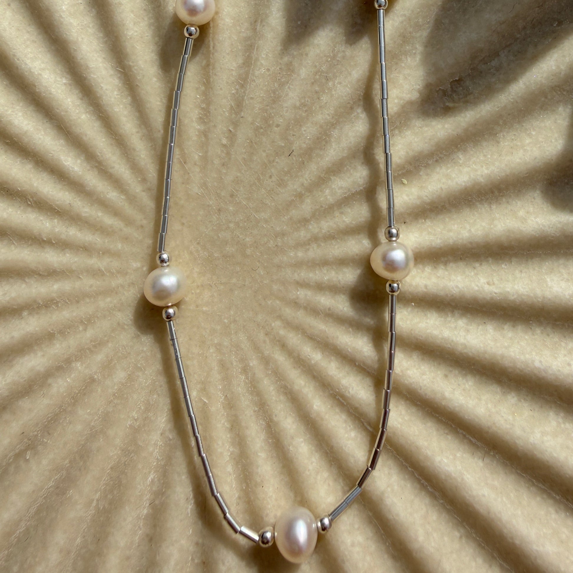 Pearl necklace on a textured beige surface with a sunburst pattern