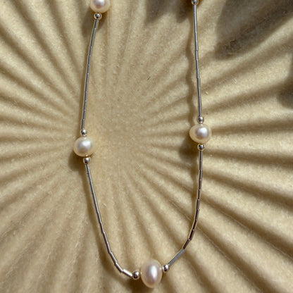 Pearl necklace on a textured beige surface with a sunburst pattern