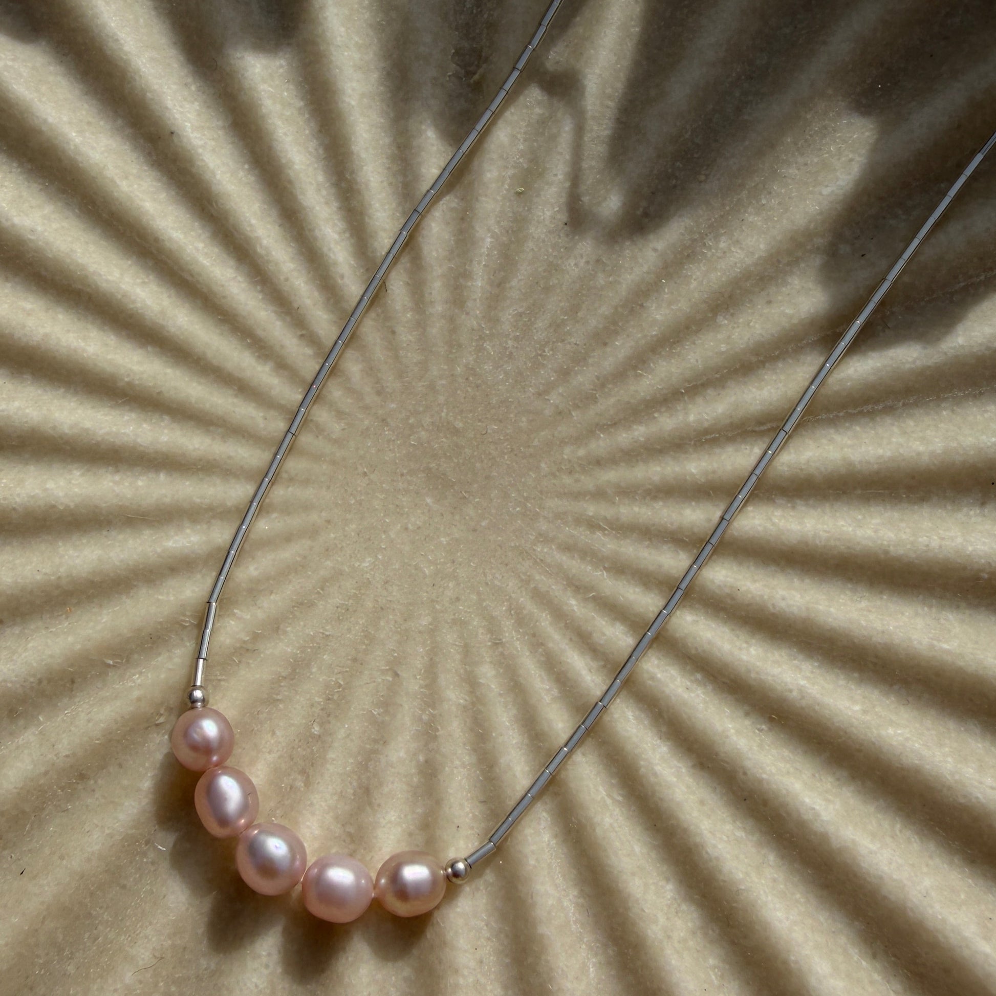 Pearl necklace on a textured beige surface with a sunburst pattern
