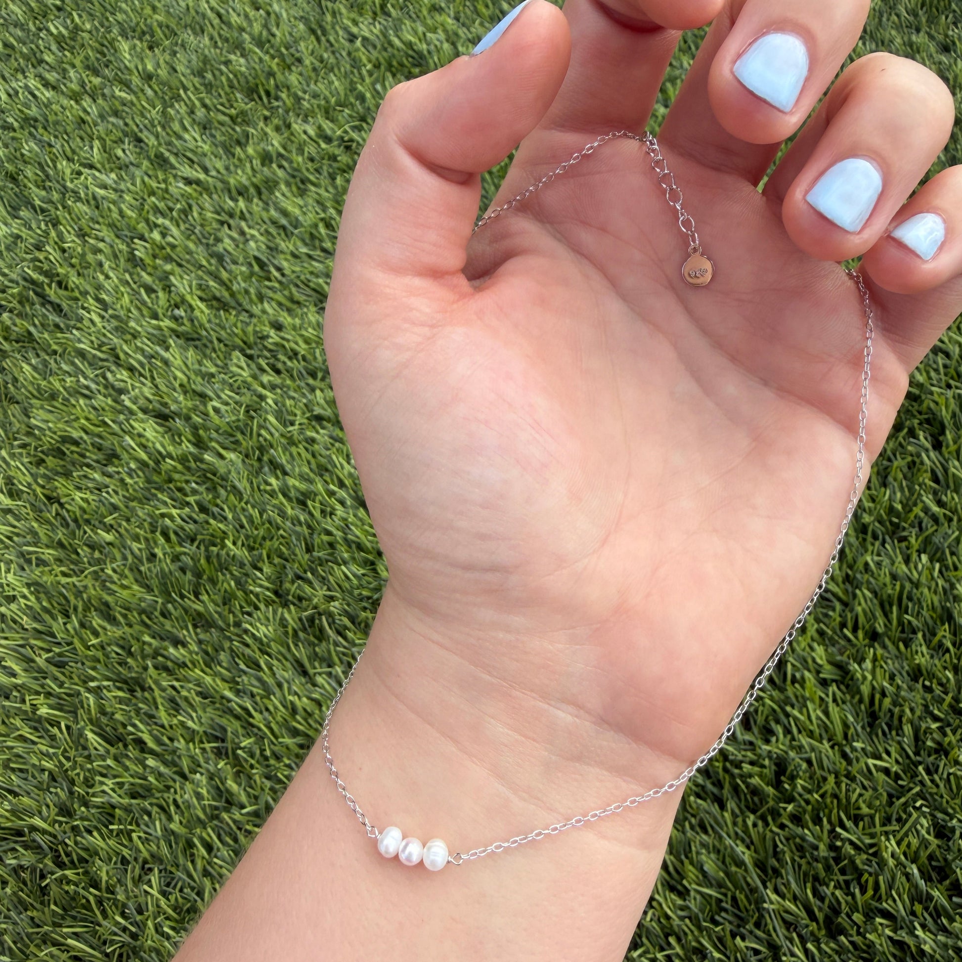 Hand wearing a delicate bracelet on a grass background