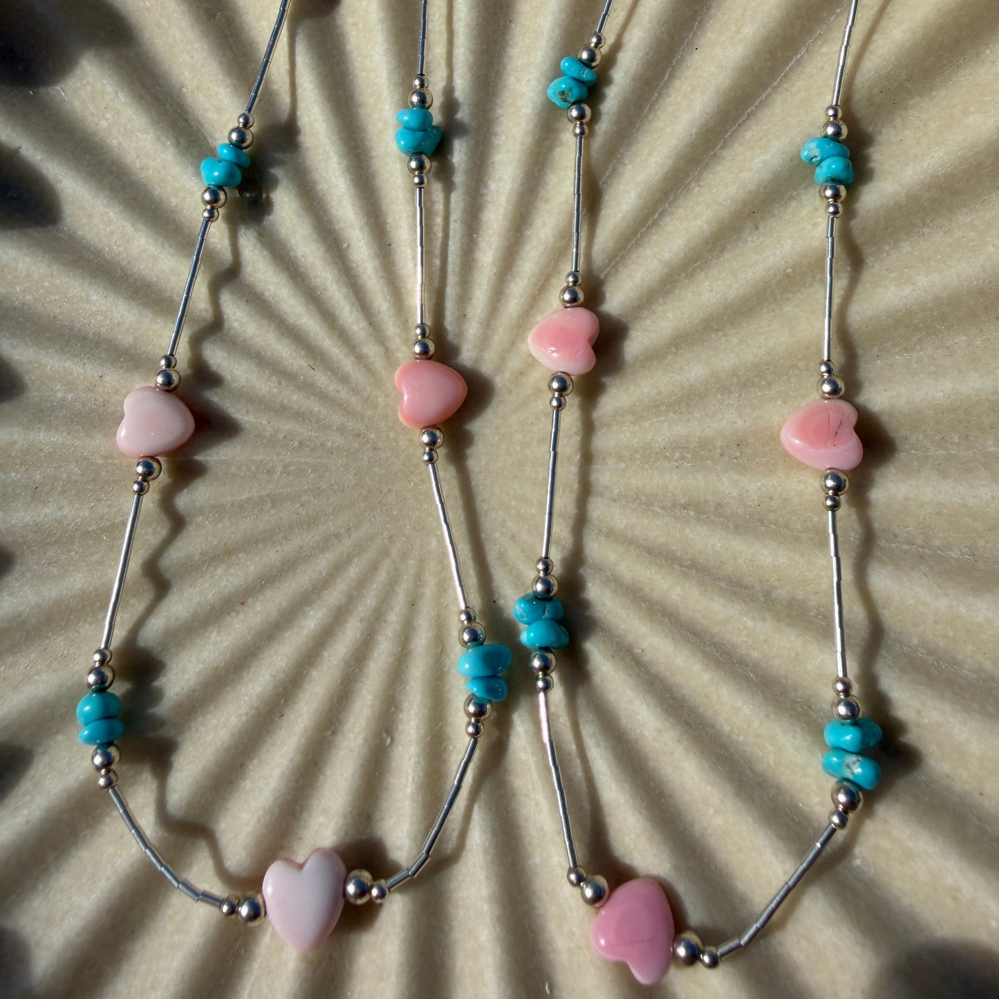 Necklace with heart-shaped pink beads and turquoise accents on a textured surface