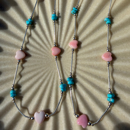 Necklace with heart-shaped pink beads and turquoise accents on a textured surface