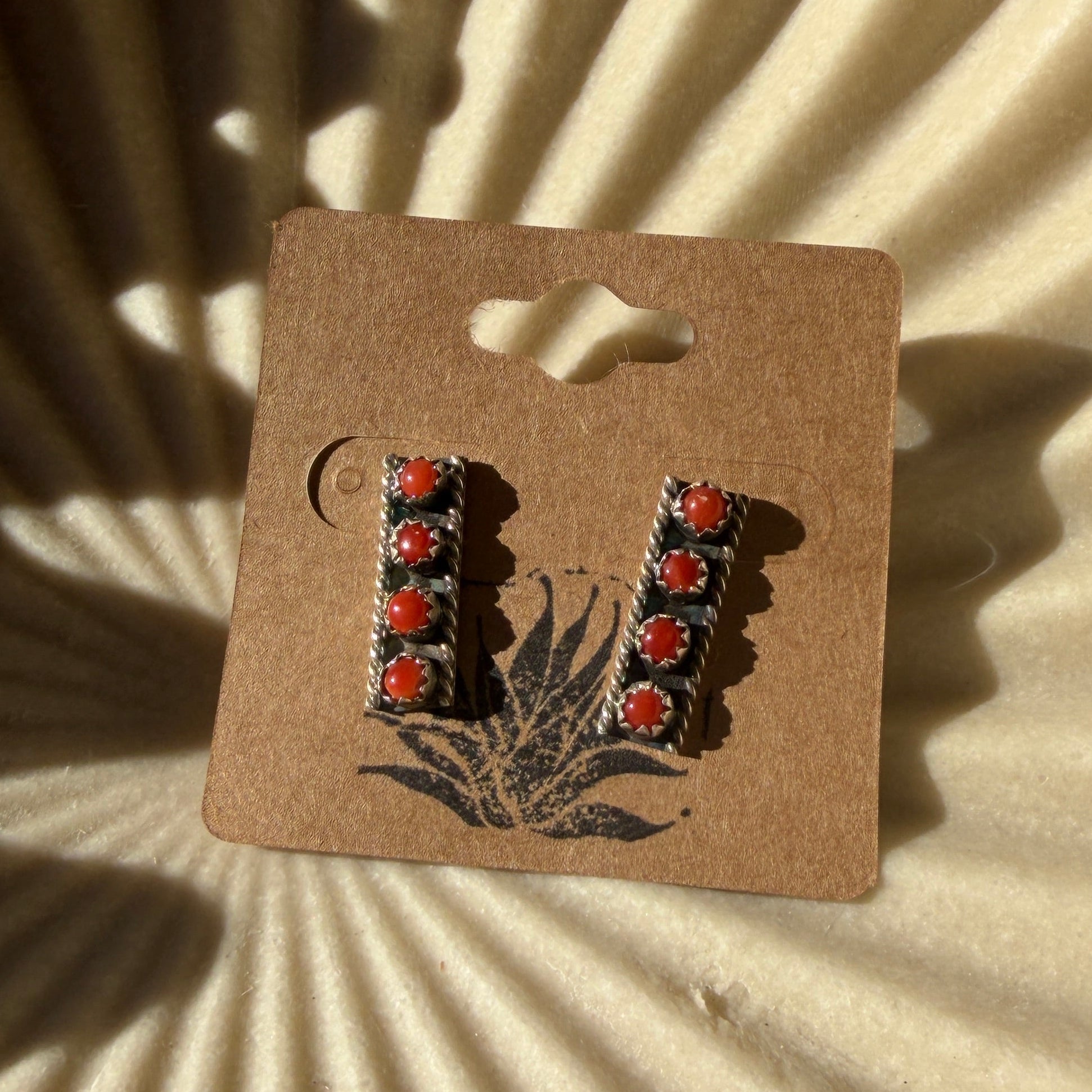 Red coral earrings on a textured beige background