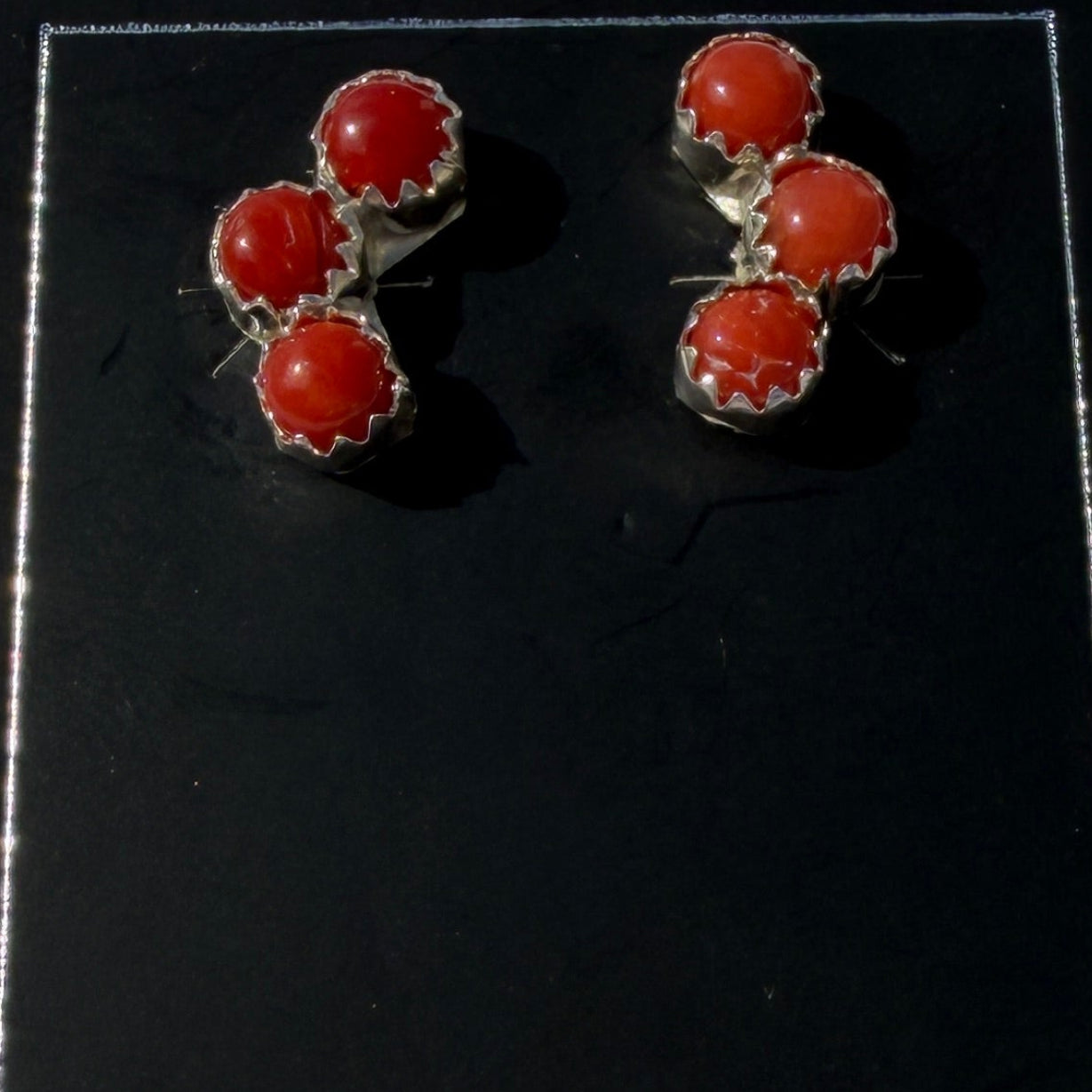 Pair of red earrings on a black card with a white border against a light gray background