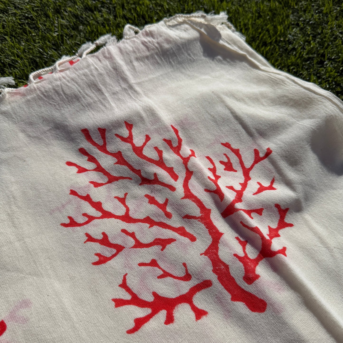 White fabric with red coral pattern on a grassy background