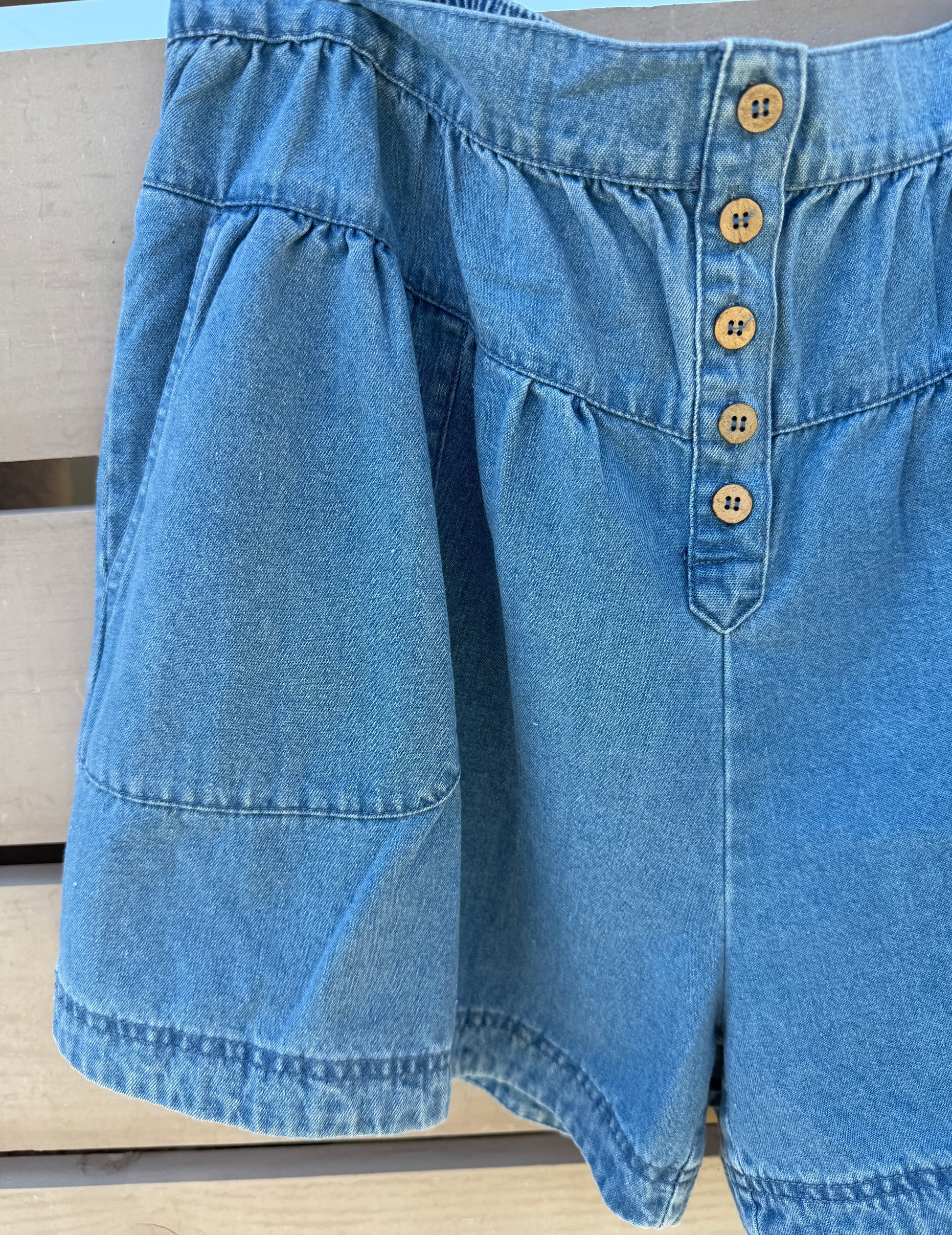 Close-up of blue denim shorts with button details on a wooden surface