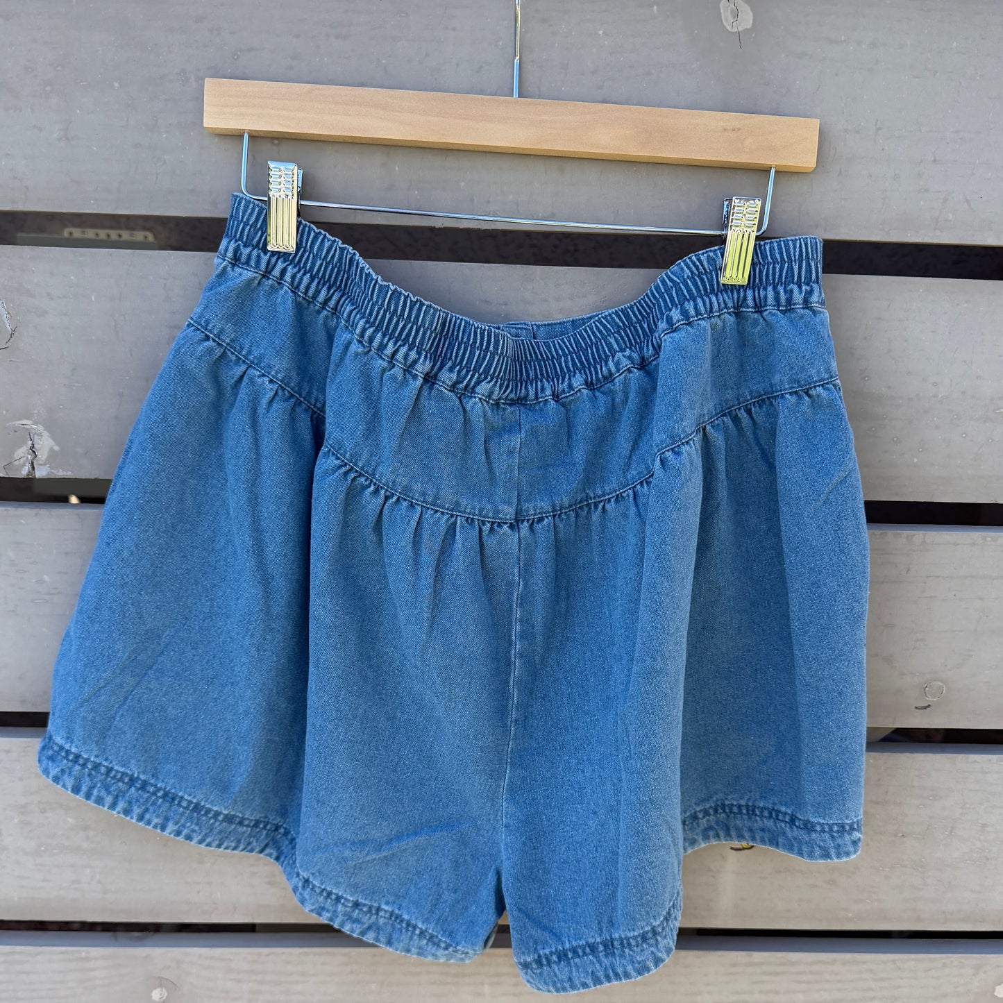 Blue denim shorts hanging on a wooden hanger against a wooden background