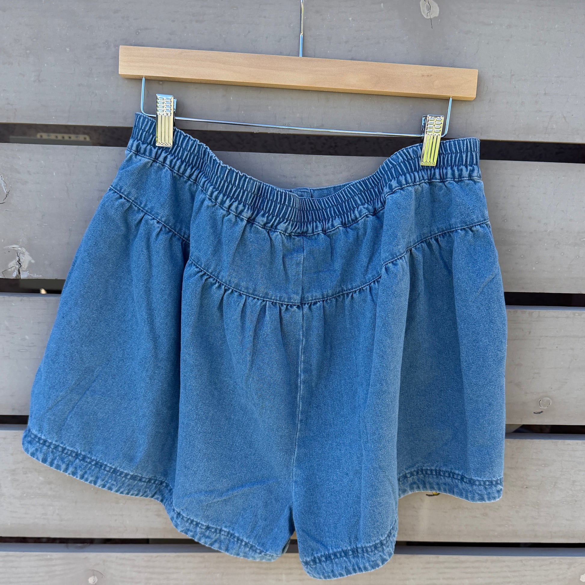 Blue denim shorts hanging on a wooden hanger against a wooden background