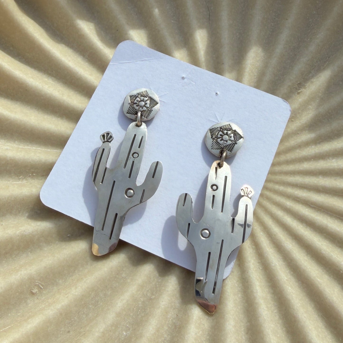 Pair of silver hand-shaped earrings on a white card against a beige textured background.