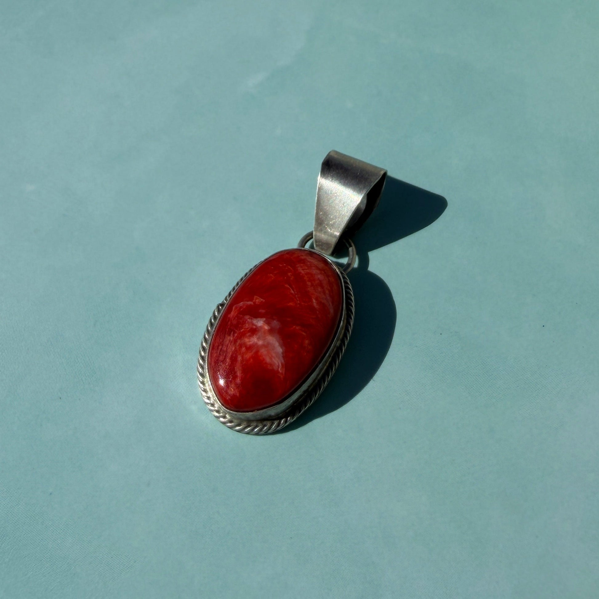 Silver pendant with a red stone on a light green surface
