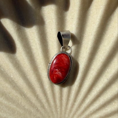 Silver pendant with a red stone on a textured beige surface
