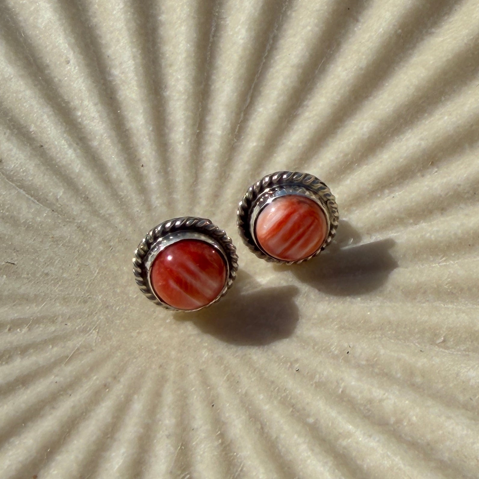 Pair of earrings with red stones on a textured beige surface