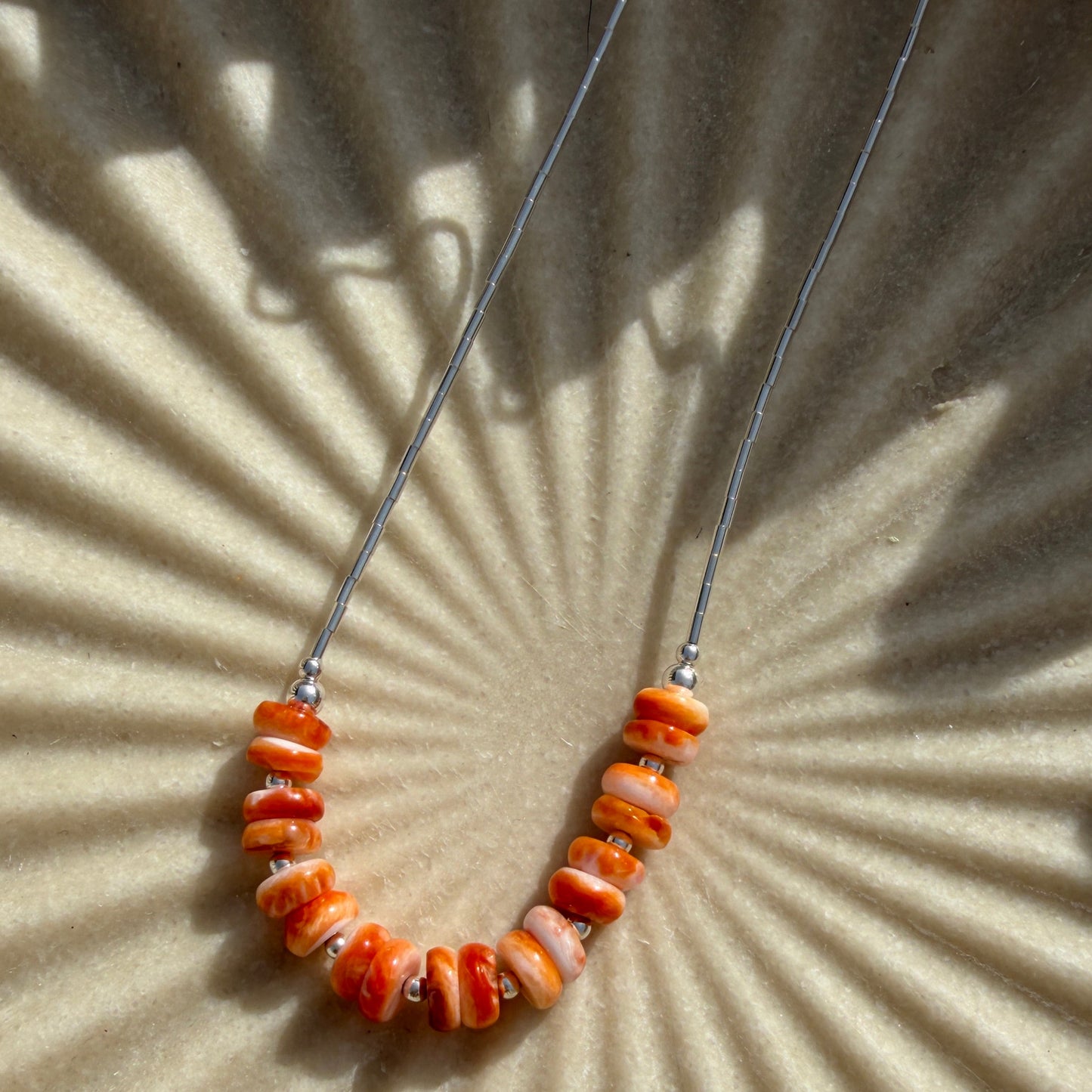 Beaded necklace with orange beads on a beige textured background