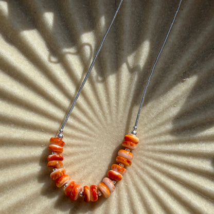 Beaded necklace with orange beads on a beige textured background