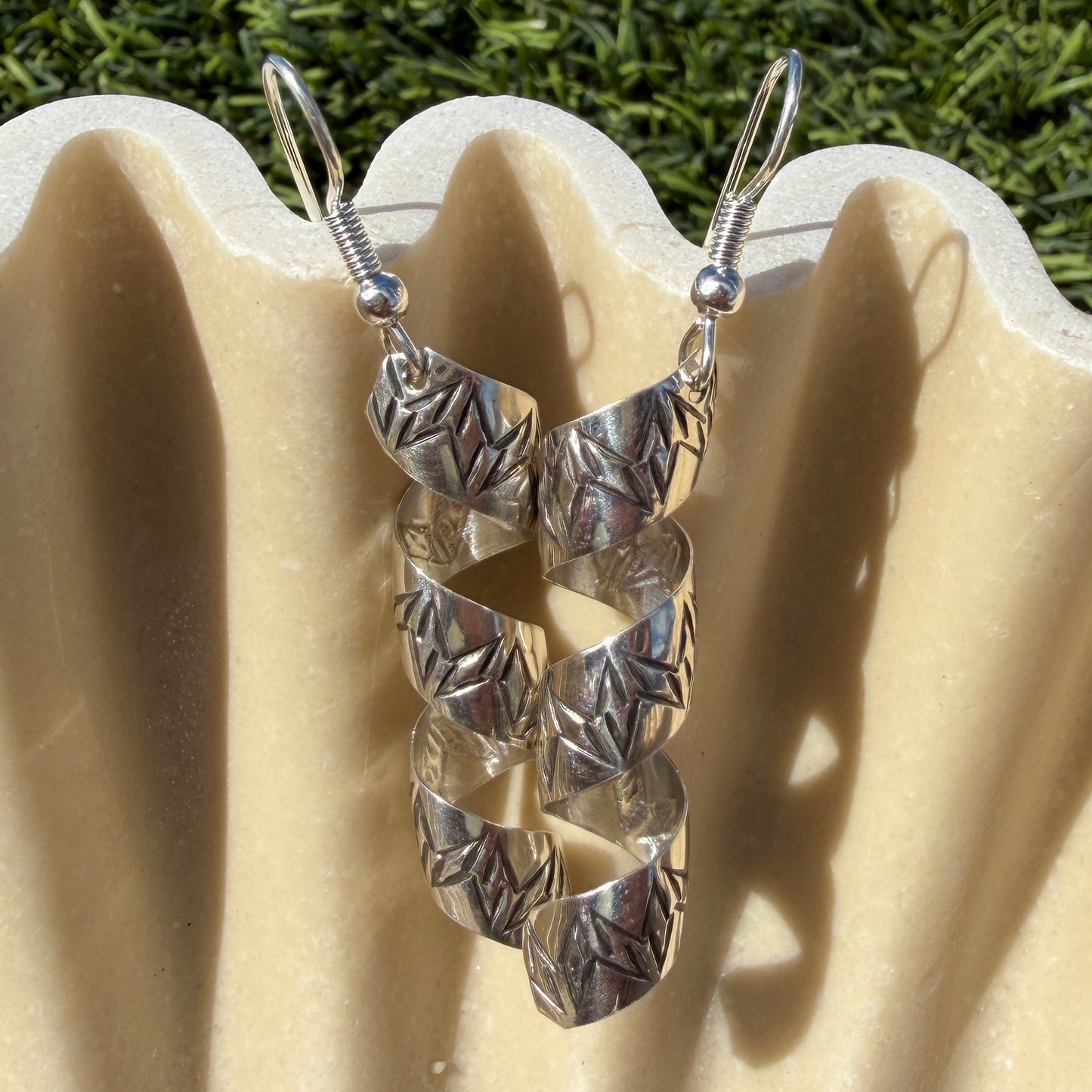 Silver spiral earrings on a beige shell with grass background