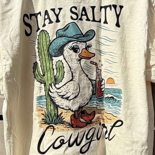 Beige tshirt with graphic design and text on a wooden deck with blue sky background