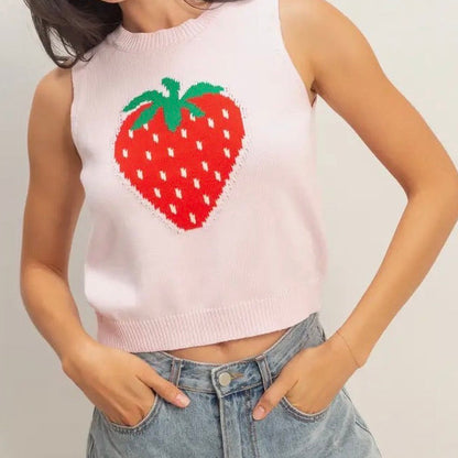 Woman wearing a sleeveless top with a strawberry design and denim shorts on a plain background