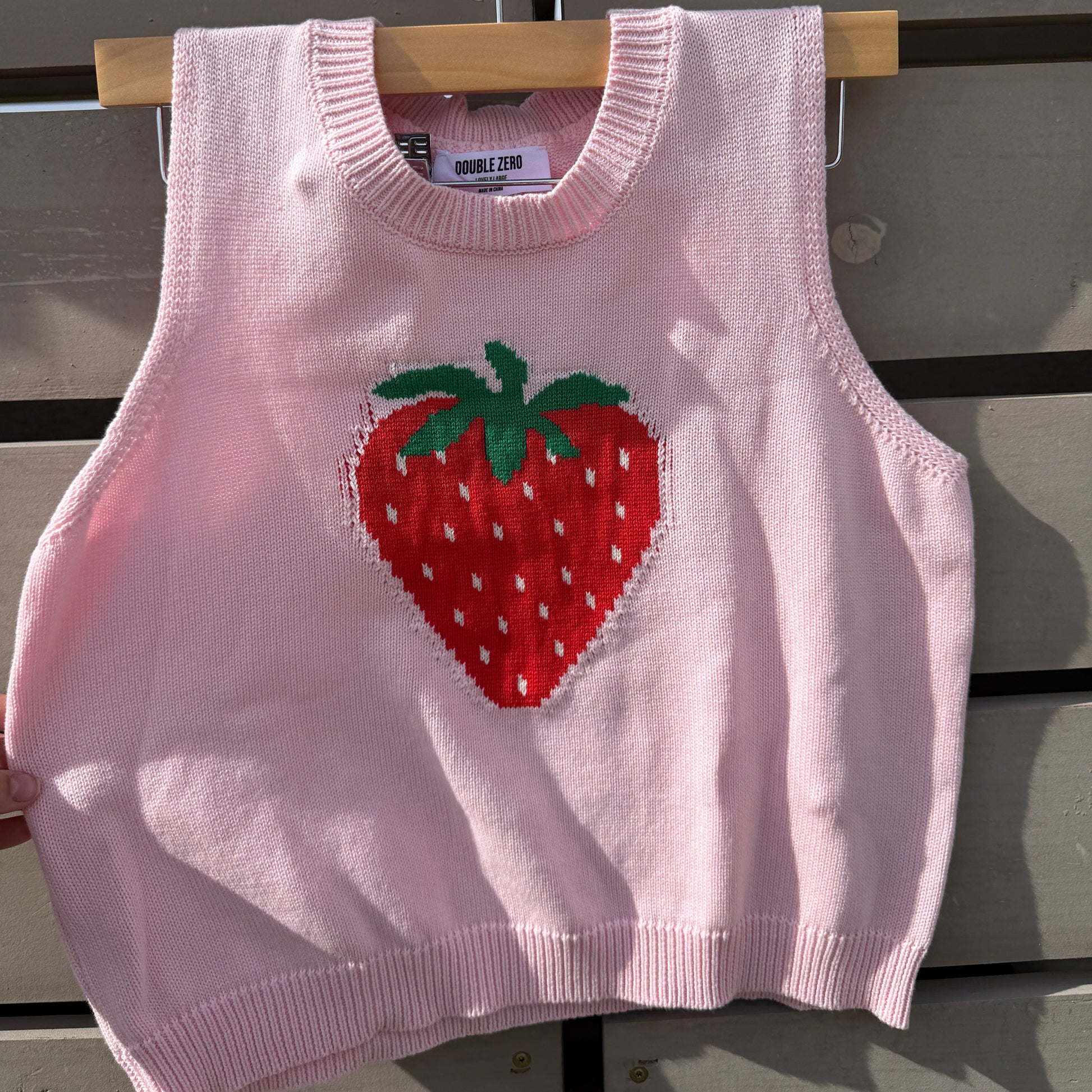 Pink sweater vest with a strawberry design on a metal surface