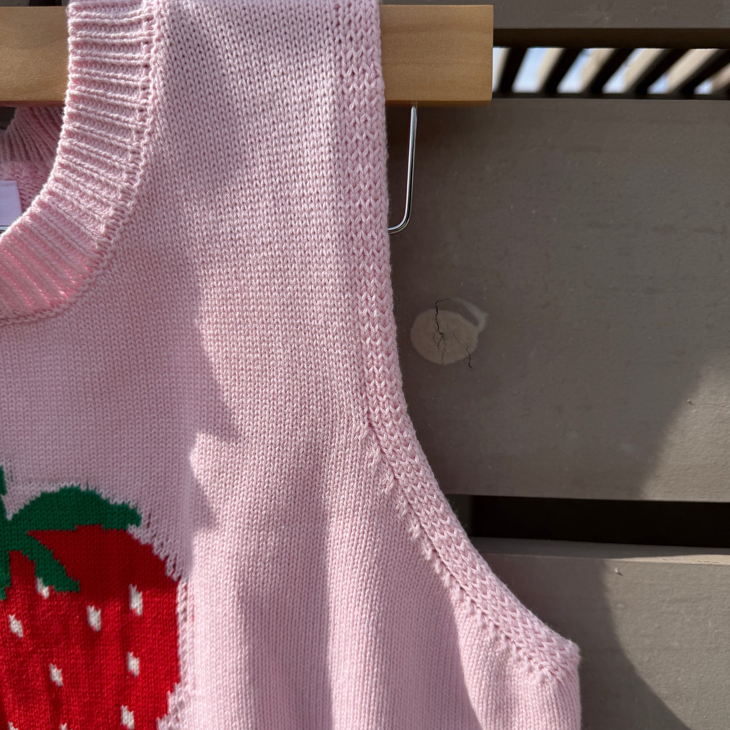 Close-up of a pink knitted garment with a red rose design on a wooden stand.