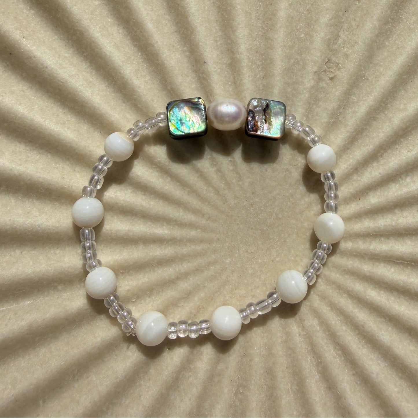 Bracelet with pearls and a central gemstone on a textured beige background