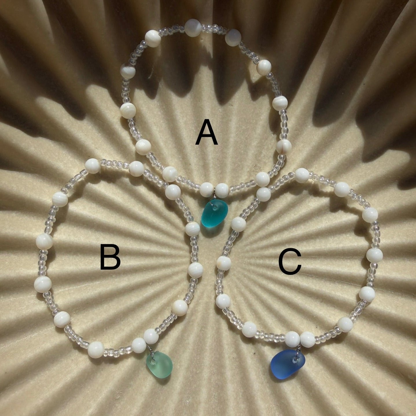 Three white beaded bracelets with colored stones on a beige textured background