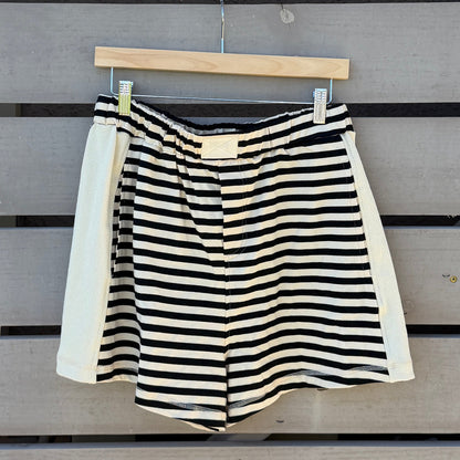 Black and white striped shorts hanging on a wooden wall with a striped awning above.