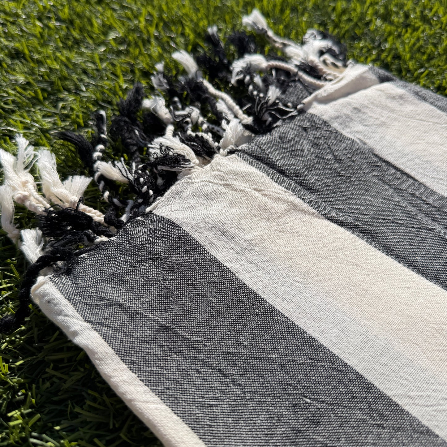 Striped towel with tassels on a grassy surface