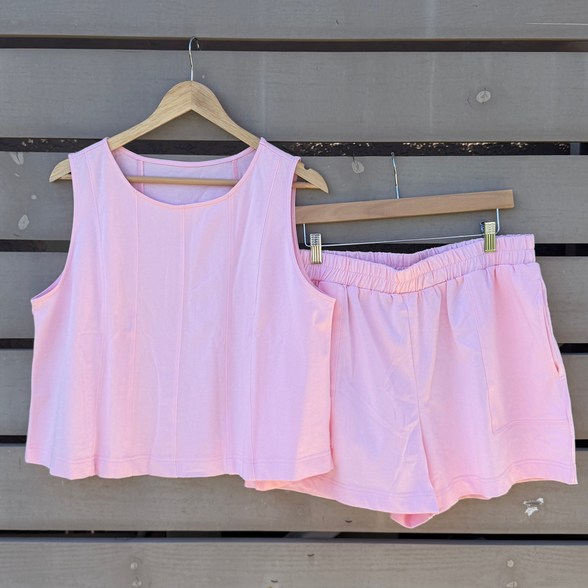 Pink sleeveless top and shorts hanging on a wooden wall with a striped awning above.