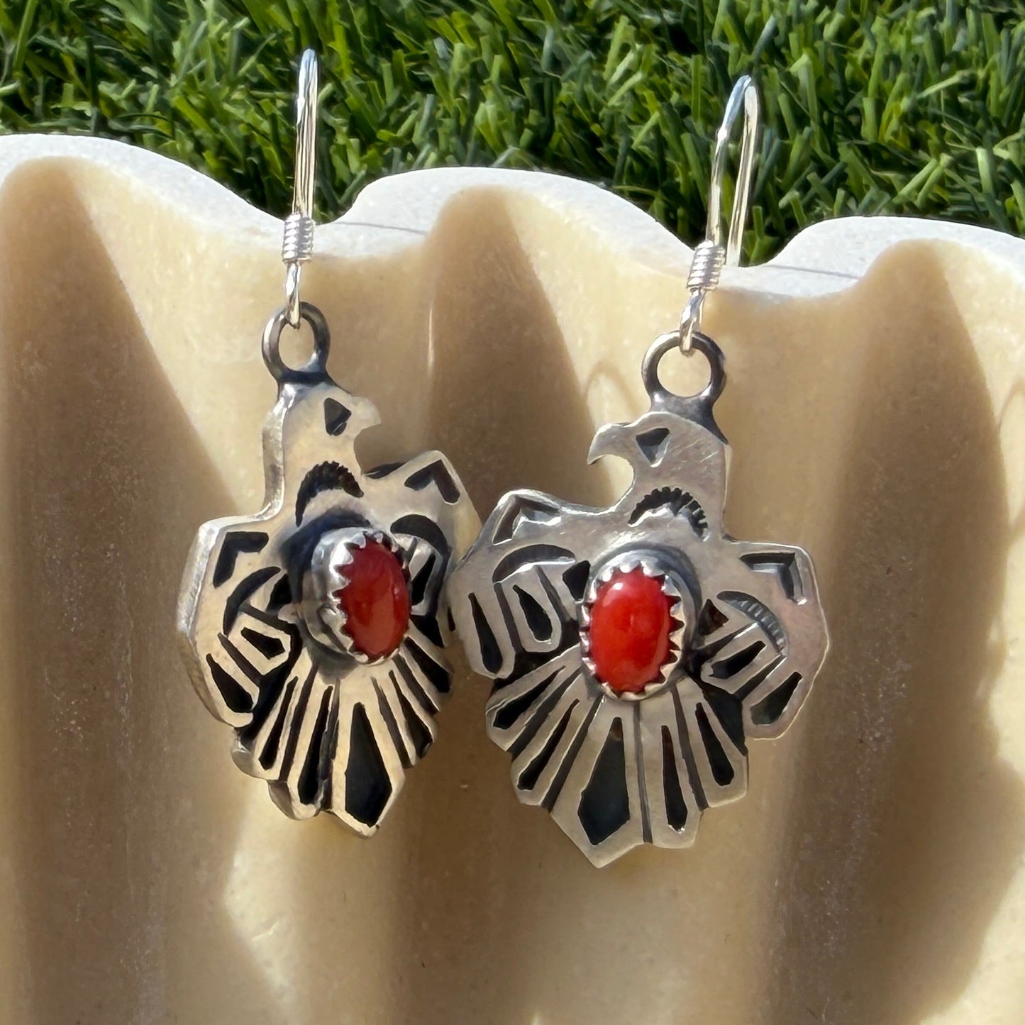 Pair of silver earrings with red stones on a beige surface with grass in the background
