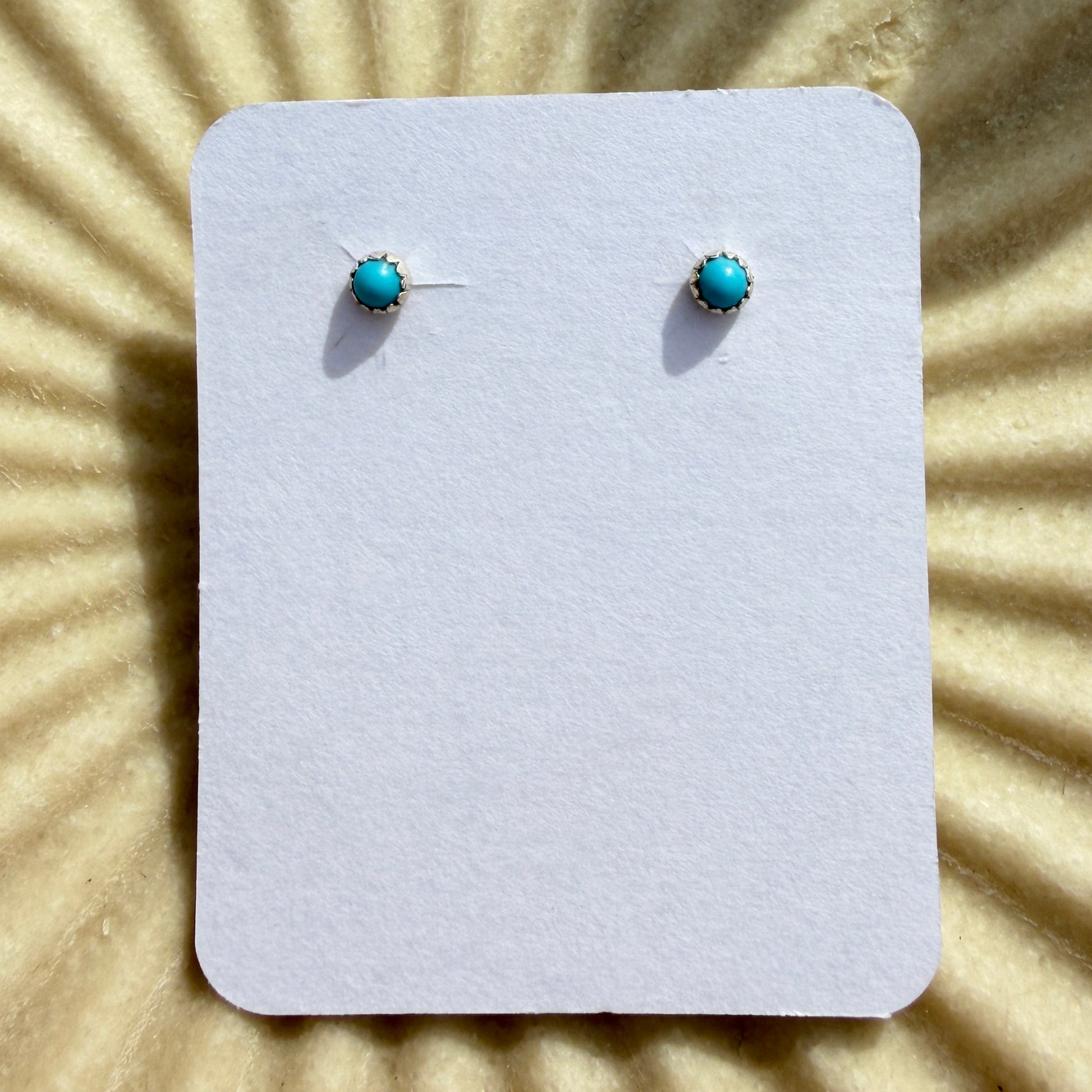 Pair of turquoise stud earrings on a white card against a beige background with sunburst pattern
