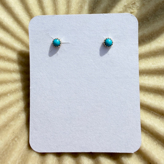 Pair of turquoise stud earrings on a white card against a beige background with sunburst pattern