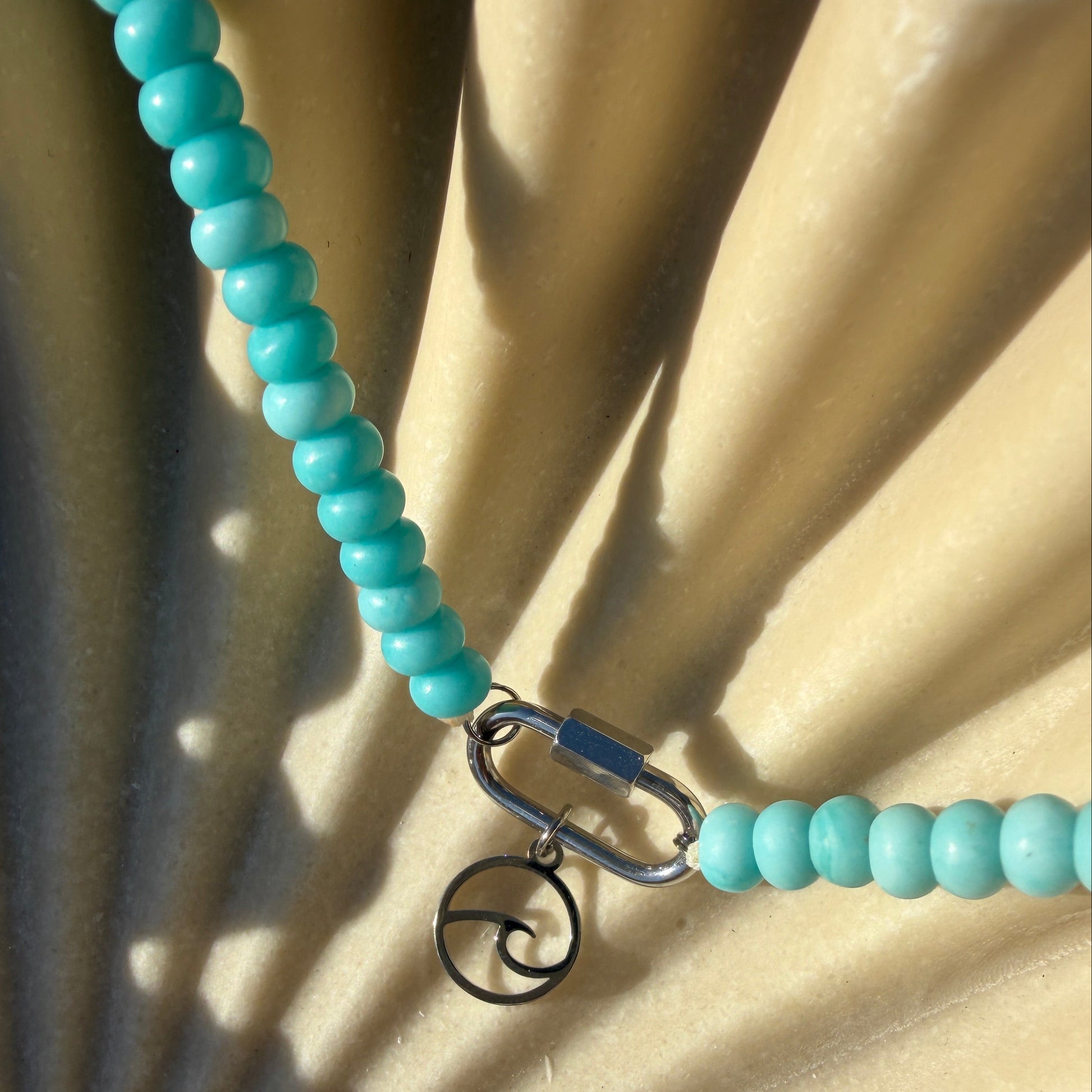 Turquoise beaded necklace with a metal clasp on a textured beige surface