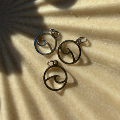 Three stainless steel wave charms on a textured beige surface
