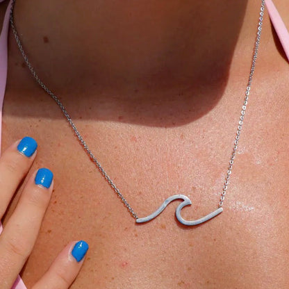 Silver wave-shaped necklace on a person wearing a pink top with blue nail polish.